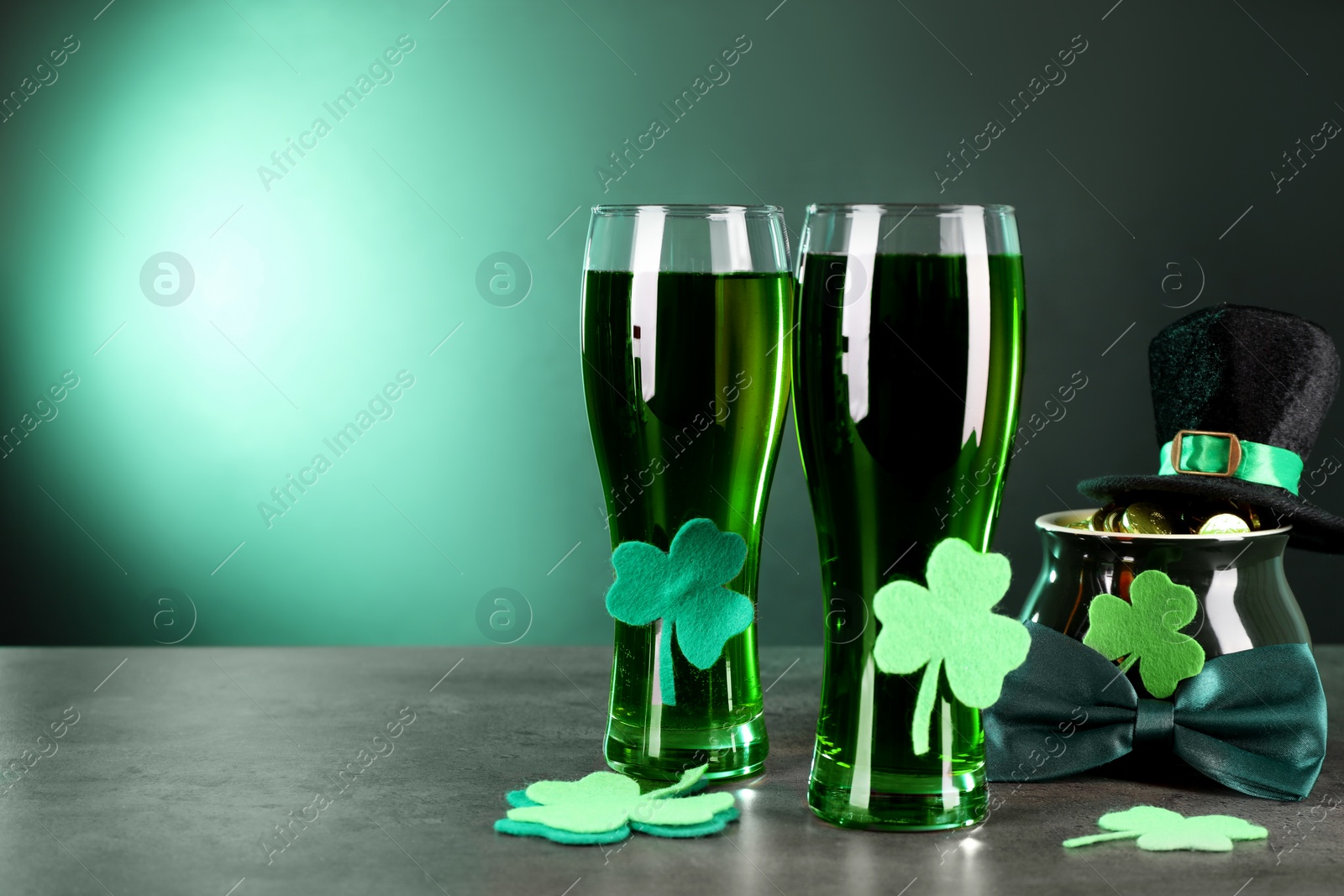 Photo of St. Patrick's day celebration. Green beer, leprechaun hat, pot of gold and decorative clover leaves on grey table. Space for text