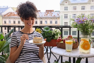 Photo of Young woman eating piece of cake on balcony with beautiful houseplants