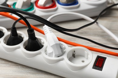 Photo of Power strip with extension cords on white wooden floor, closeup. Electrician's equipment