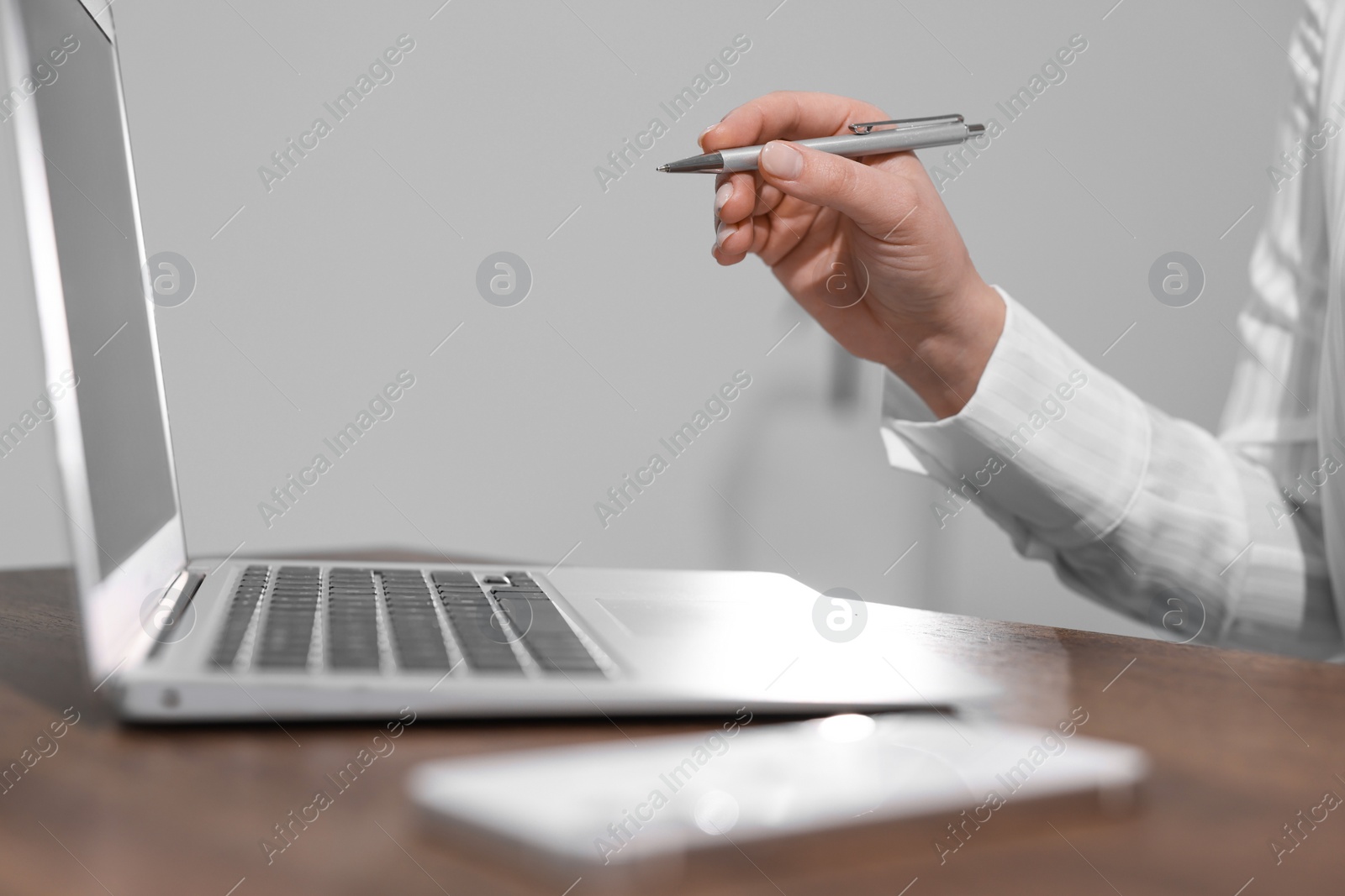 Photo of Woman with smartphone and pen working on laptop at wooden table, closeup. Electronic document management