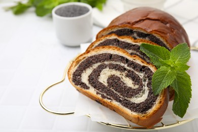 Photo of Slices of poppy seed roll and mint on white tiled table, closeup with space for text. Tasty cake