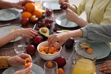 Photo of Vegetarian food. Friends eating fresh fruits at wooden table indoors, closeup