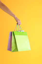Photo of Woman with paper shopping bags on yellow background, closeup