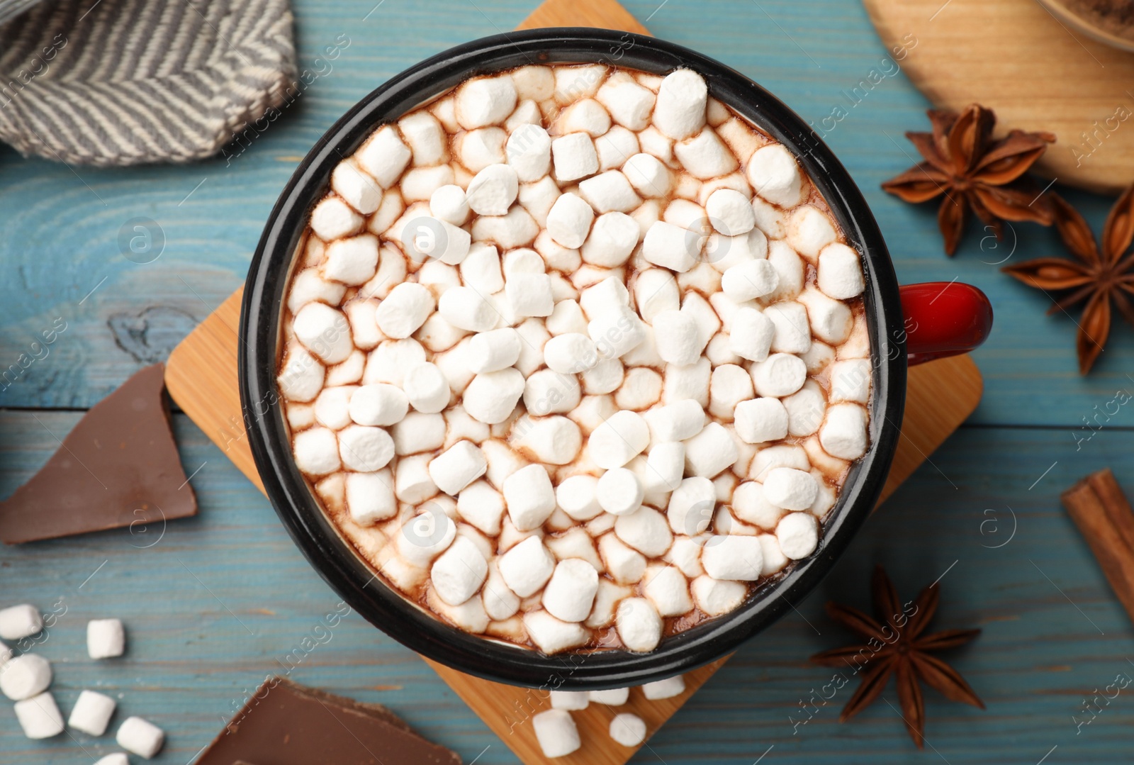 Photo of Tasty hot chocolate with marshmallows and ingredients on light blue wooden table, flat lay