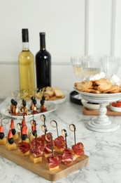 Different tasty canapes on white marble table, closeup