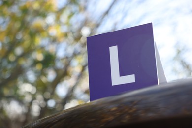 Photo of L-plate on car outdoors, low angle view with space for text. Driving school