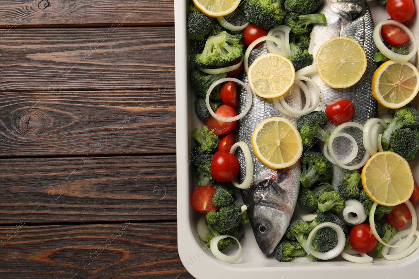 Photo of Raw fish with vegetables and lemon in baking dish on wooden table, top view. Space for text