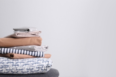 Photo of Stack of clean bed linen and pillow on light grey background. Space for text