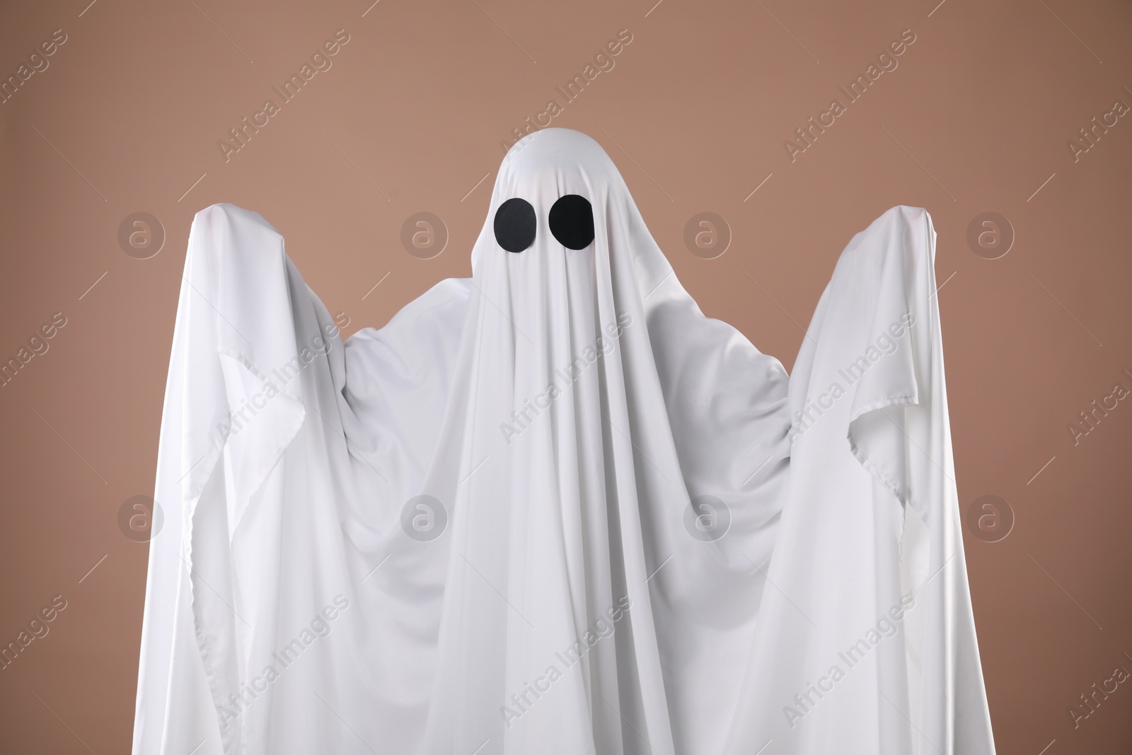 Photo of Creepy ghost. Person covered with white sheet on dark beige background