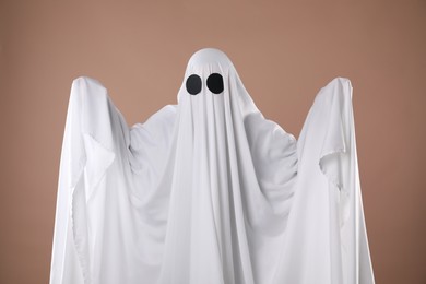 Creepy ghost. Person covered with white sheet on dark beige background