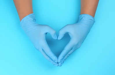 Photo of Person in latex gloves showing heart gesture against light blue background, closeup on hands