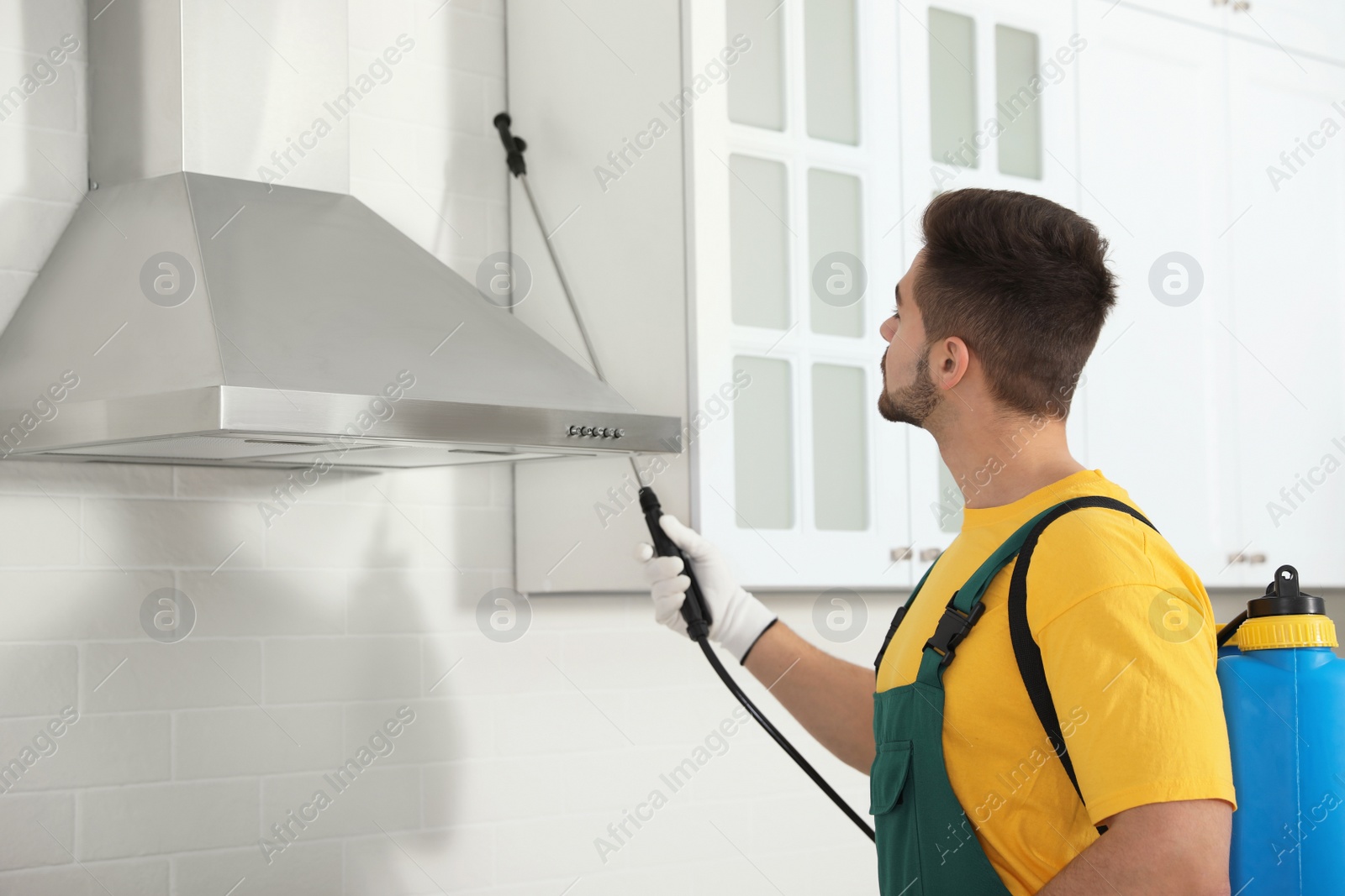 Photo of Pest control worker spraying insecticide on furniture in kitchen