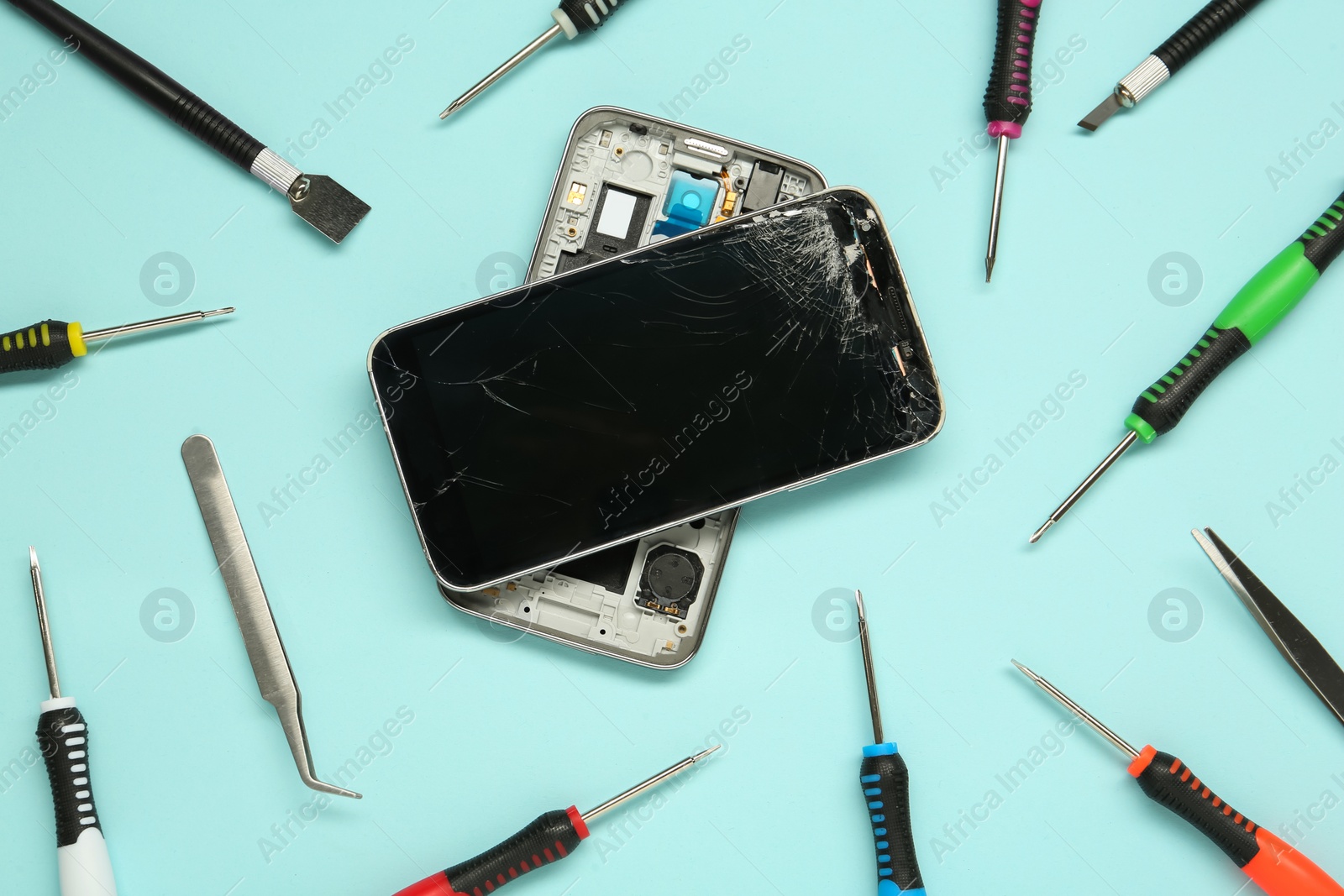 Photo of Damaged smartphone and repair tool set on light blue background, flat lay