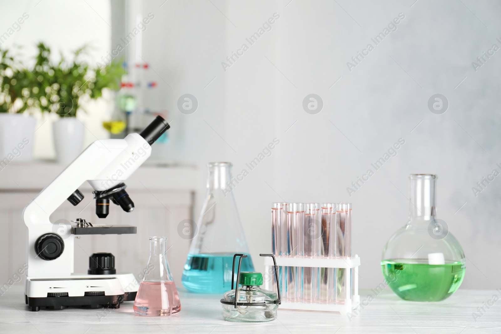 Photo of Laboratory glassware and microscope on table indoors. Chemistry concept