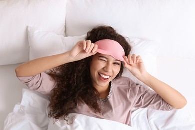 Happy African American woman with sleeping mask in bed, top view