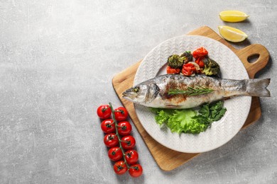 Photo of Delicious baked fish and vegetables on light grey table, top view. Space for text