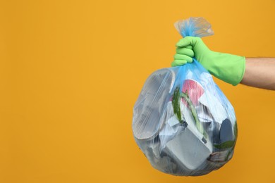 Photo of Man holding full garbage bag on yellow background, closeup. Space for text