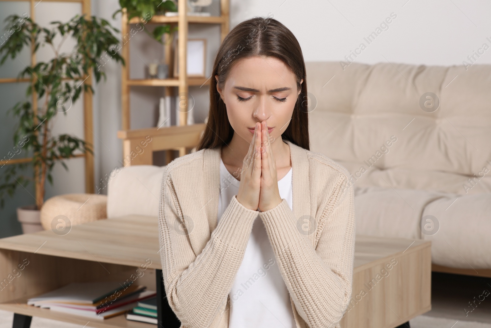 Photo of Woman with clasped hands praying at home