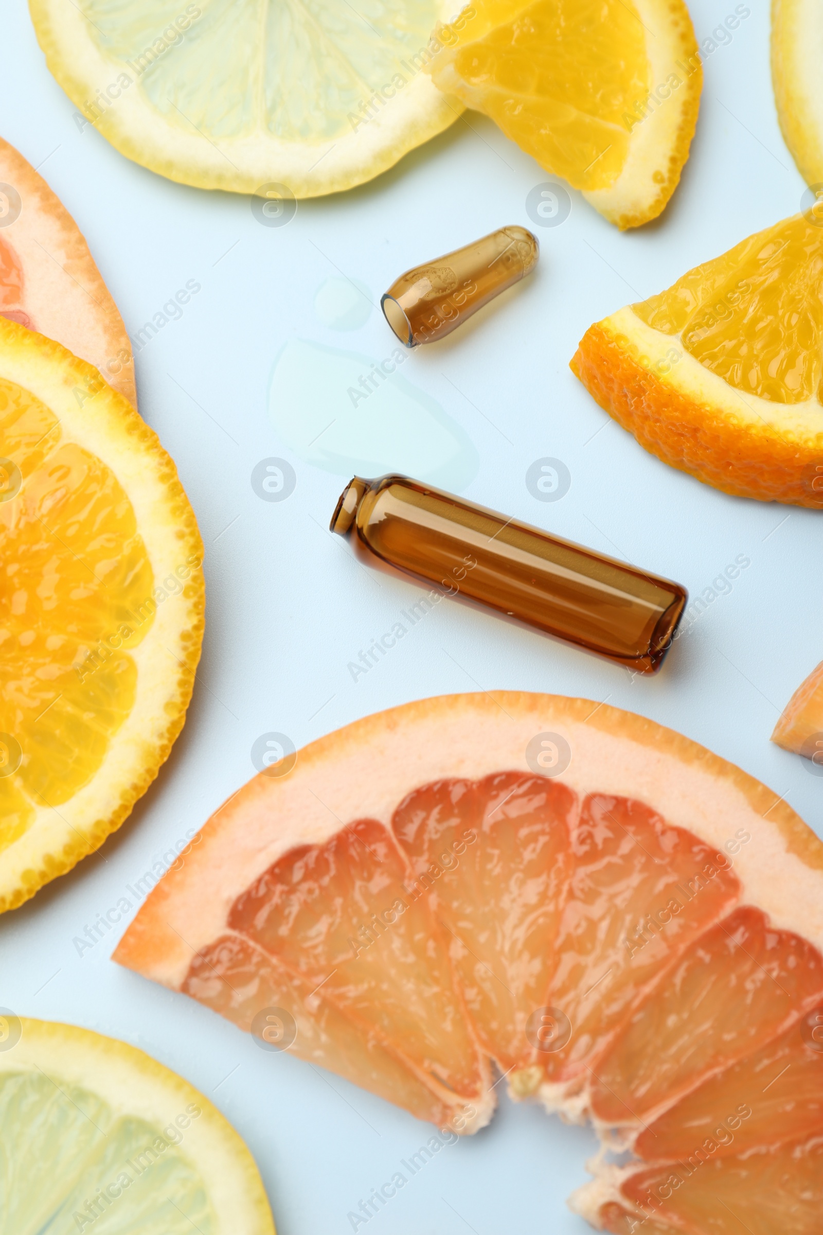 Photo of Broken skincare ampoule with vitamin C and slices of different citrus fruits on light blue background, closeup