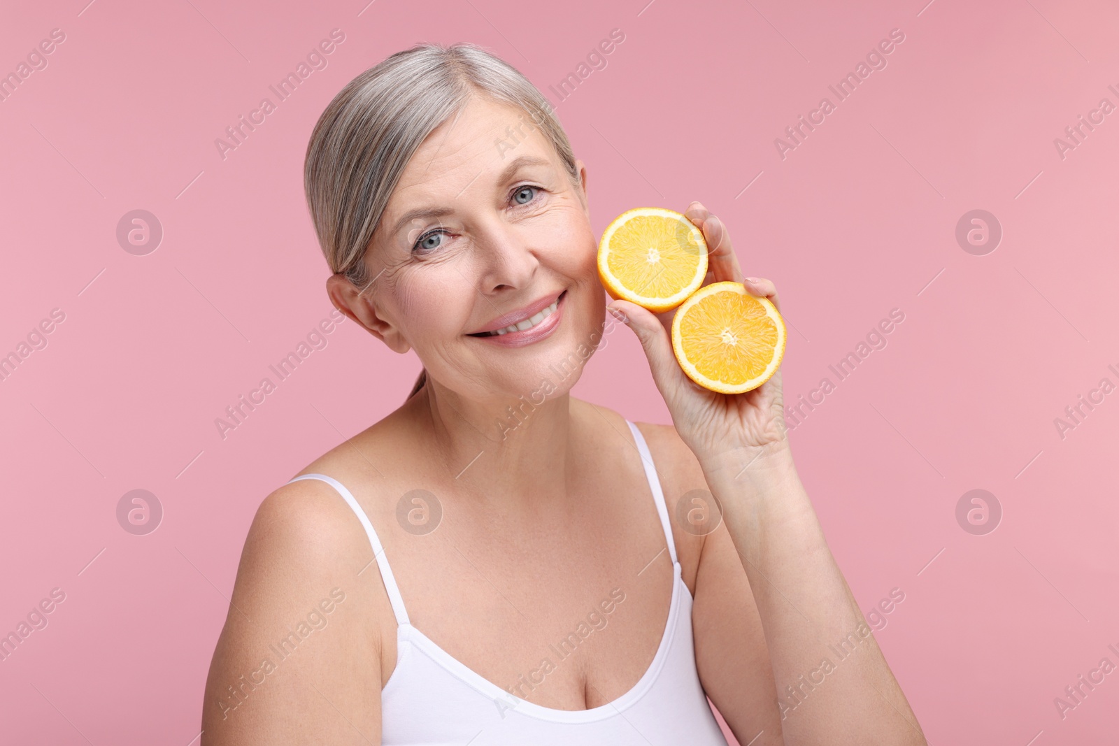 Photo of Beautiful woman with halves of orange rich in vitamin C on pink background