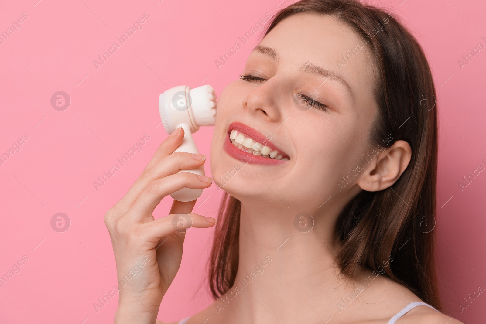 Photo of Washing face. Young woman with cleansing brush on pink background