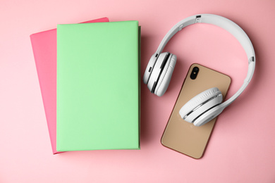 Books, mobile phone and headphones on pink background, flat lay