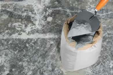 Photo of Cement powder and trowel put in bag on stone floor, above view. Space for text