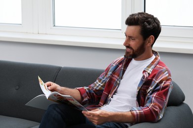 Photo of Smiling bearded man reading magazine on sofa indoors