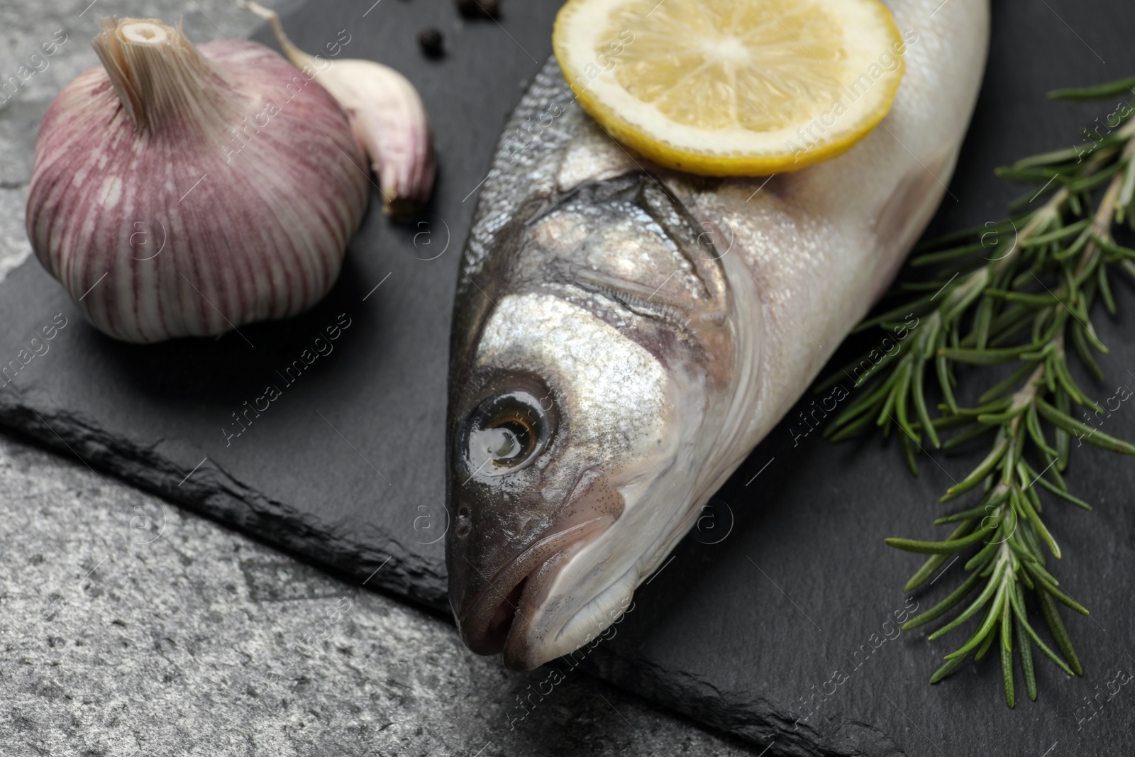 Photo of Sea bass fish and ingredients on grey table, closeup