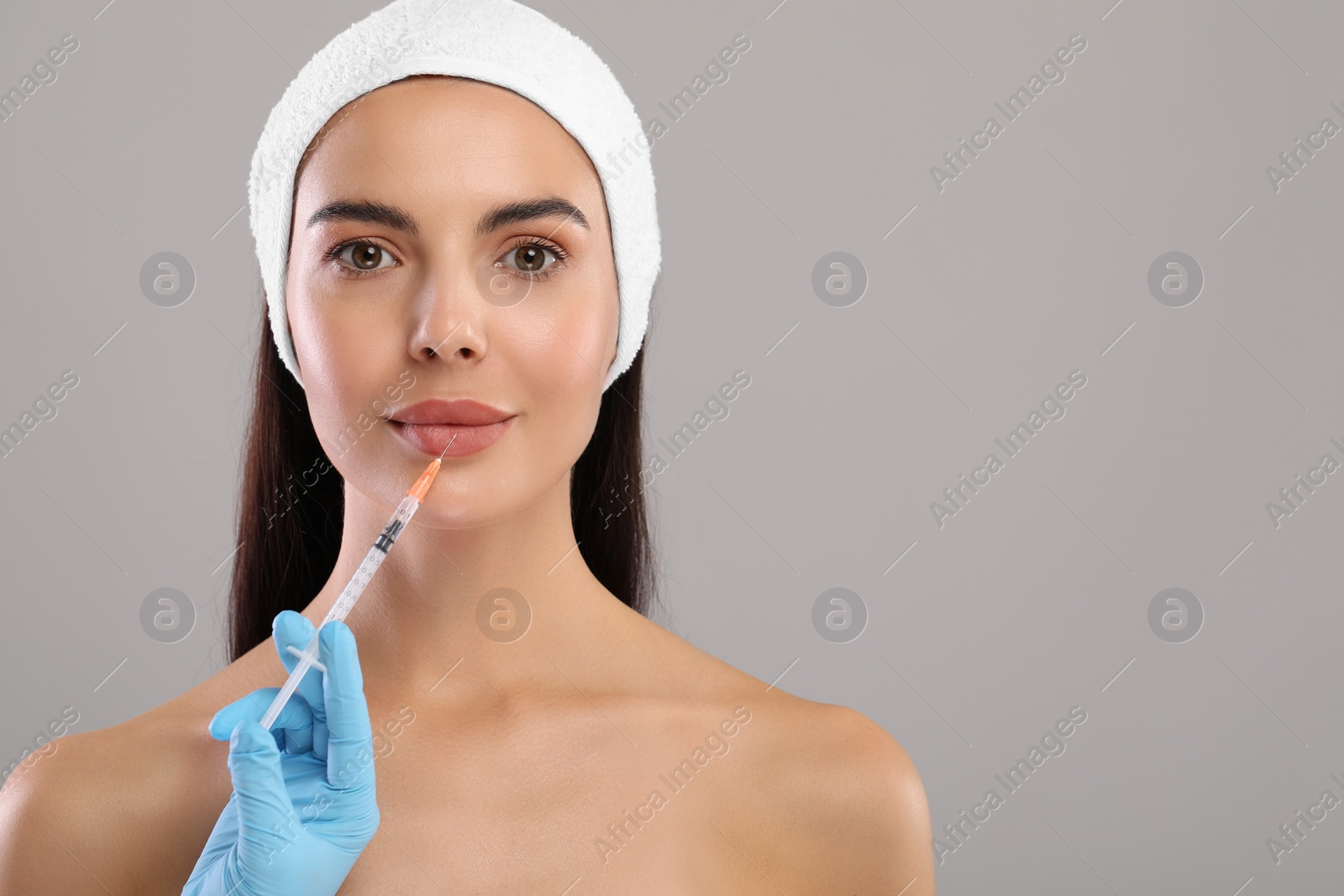 Photo of Doctor giving lips injection to young woman on light grey background, space for text. Cosmetic surgery