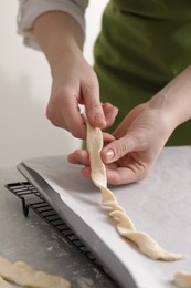 Photo of Woman putting homemade breadsticks on baking sheet at light grey marble table, closeup. Cooking traditional grissini