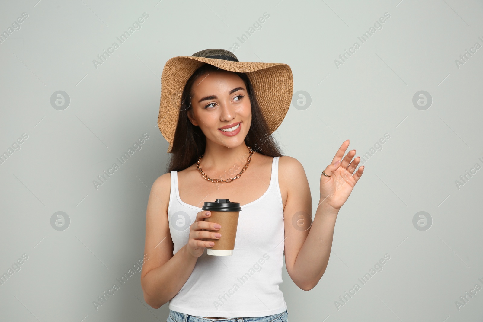 Photo of Beautiful young woman with straw hat and cup of coffee on light grey background. Stylish headdress