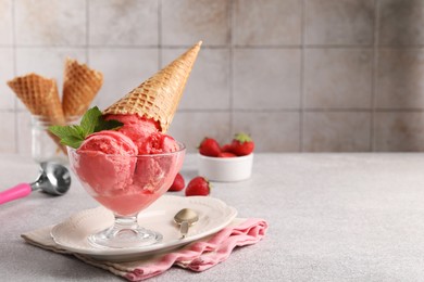 Delicious scoops of strawberry ice cream with mint and wafer cone in glass dessert bowl served on grey table. Space for text