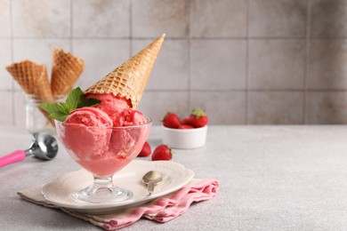 Photo of Delicious scoops of strawberry ice cream with mint and wafer cone in glass dessert bowl served on grey table. Space for text