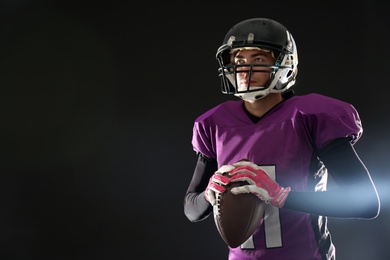 Photo of American football player with ball on dark background. Space for text
