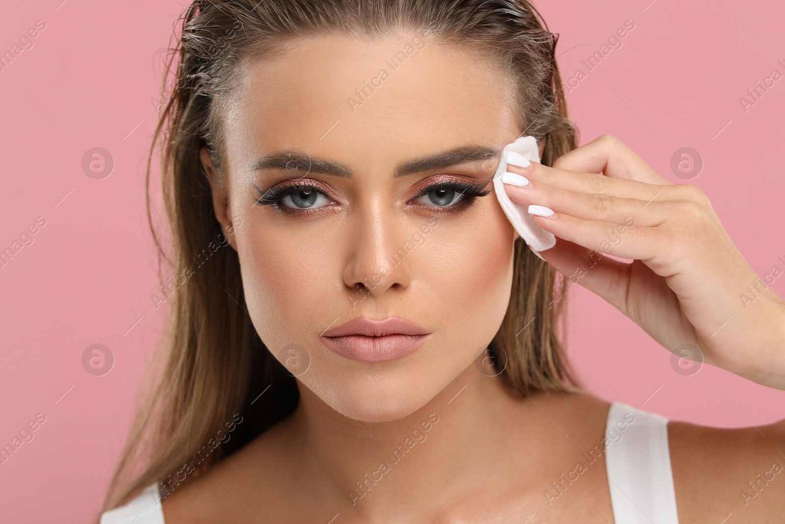 Photo of Beautiful woman removing makeup with cotton pad on pink background, closeup