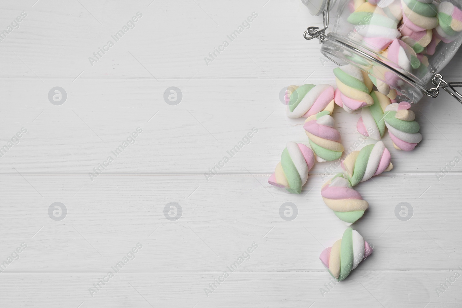 Photo of Glass jar with colorful marshmallows on white wooden table, flat lay. Space for text