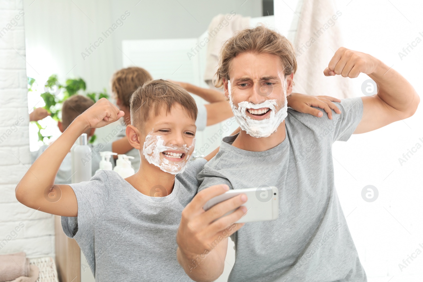 Photo of Father and son taking selfie with shaving foam on faces in bathroom