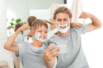 Photo of Father and son taking selfie with shaving foam on faces in bathroom