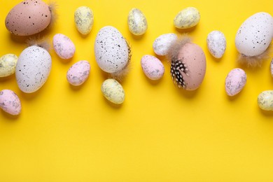 Many painted Easter eggs on yellow background, flat lay. Space for text