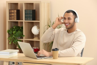 Smiling African American man in headphones working on laptop at wooden table indoors