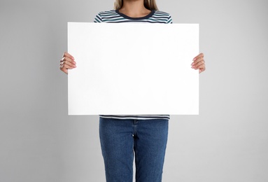 Photo of Woman holding blank poster on light grey background, closeup