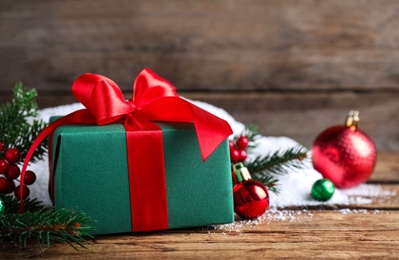 Christmas gift box with red bow and festive decor on wooden table, closeup