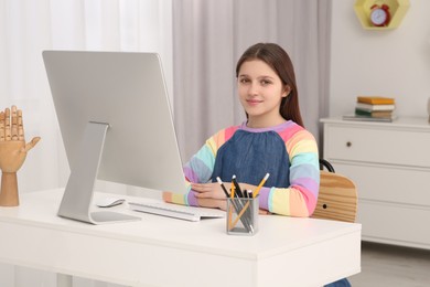 Cute girl using computer at desk in room. Home workplace