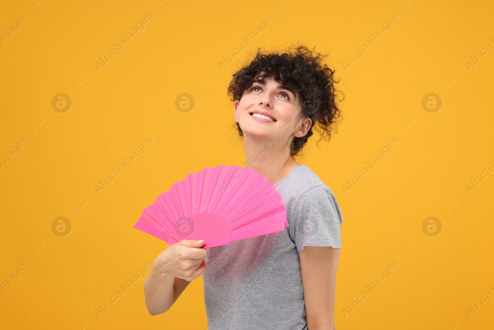 Photo of Happy woman holding hand fan on orange background