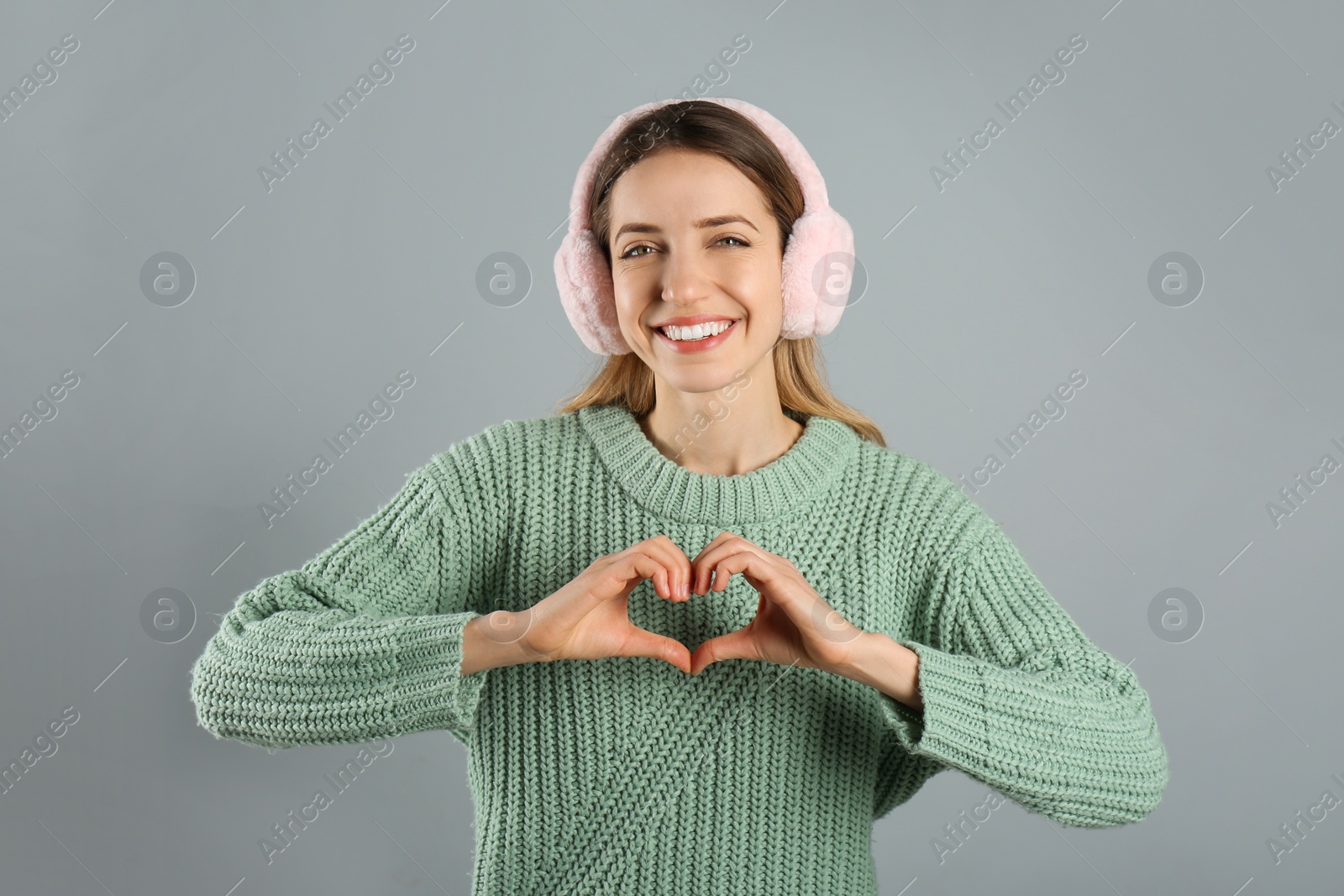 Photo of Happy woman wearing warm earmuffs on grey background