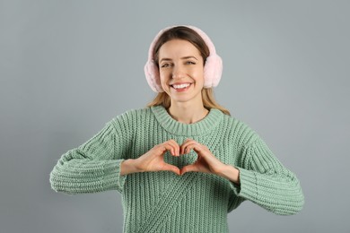 Happy woman wearing warm earmuffs on grey background