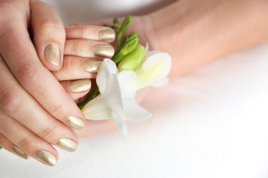 Photo of Woman with gold manicure holding flower on light background, closeup. Nail polish trends