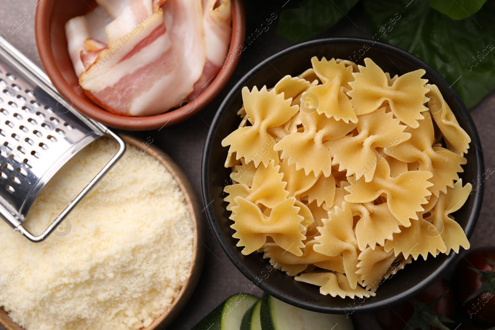 Photo of Raw pasta, bacon and fresh ingredients on brown table, flat lay