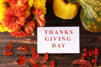 Photo of Thanksgiving day, holiday celebrated every fourth Thursday in November. Paper card, autumn leaves, berries, quince and pumpkin on wooden table, flat lay